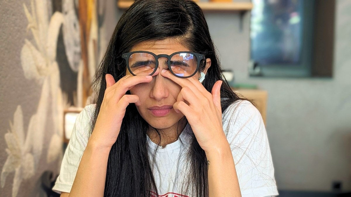 une Femme portant des lunettes, se pinçant l’arête du nez avec une expression de fatigue oculaire.
